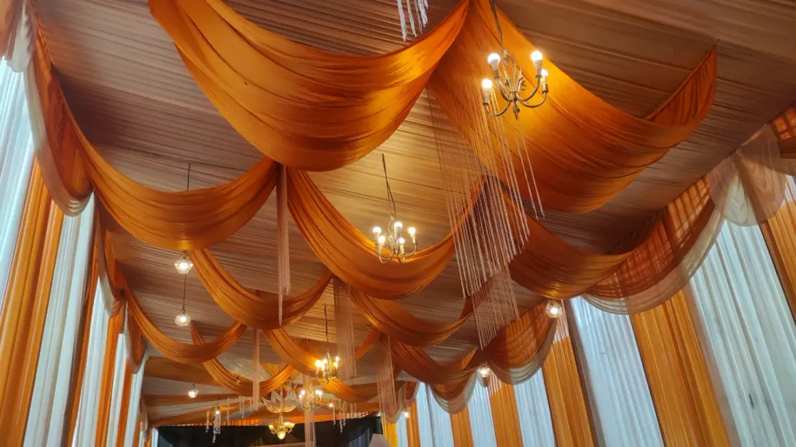 Techo con telas naranjas y blancas, adornado con candelabros y colgantes de cristal.