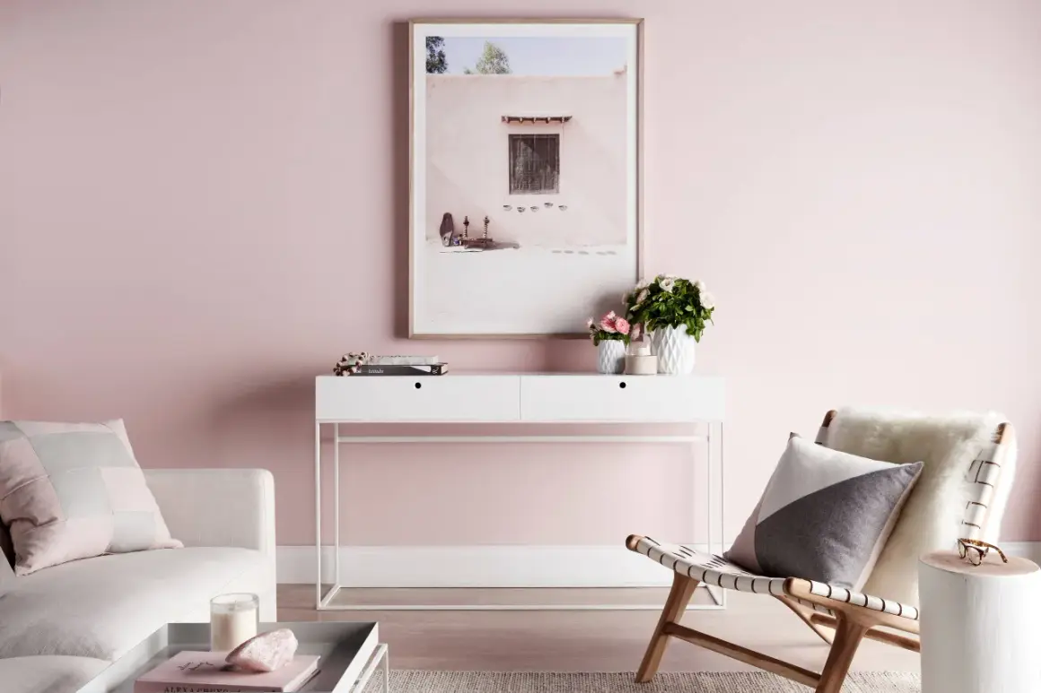 Un salón con paredes rosas, un sofá blanco, una consola con flores y un cuadro. El rosa se combina con blanco, gris y madera para un ambiente sereno.