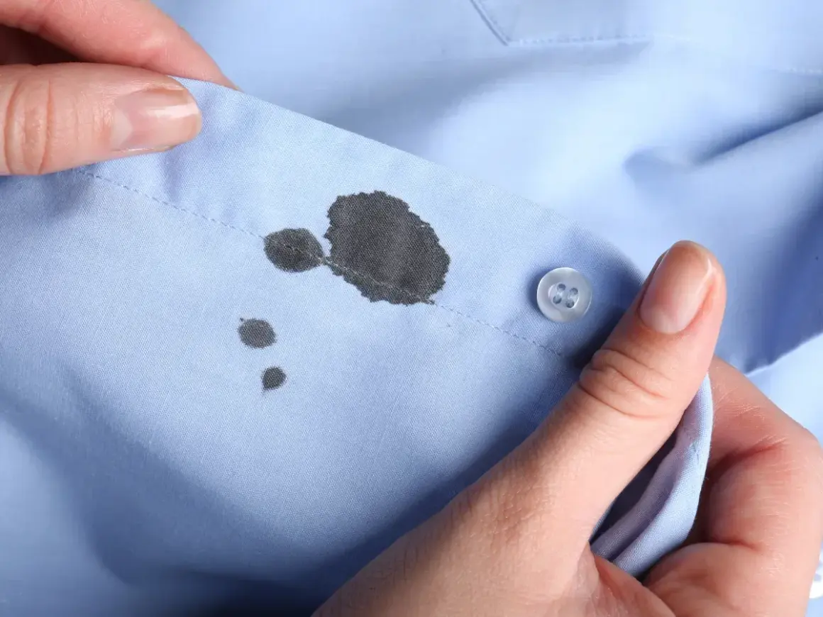 Manos sujetan camisa azul con manchas de boli. Aprende como quitar manchas de boli fácilmente.
