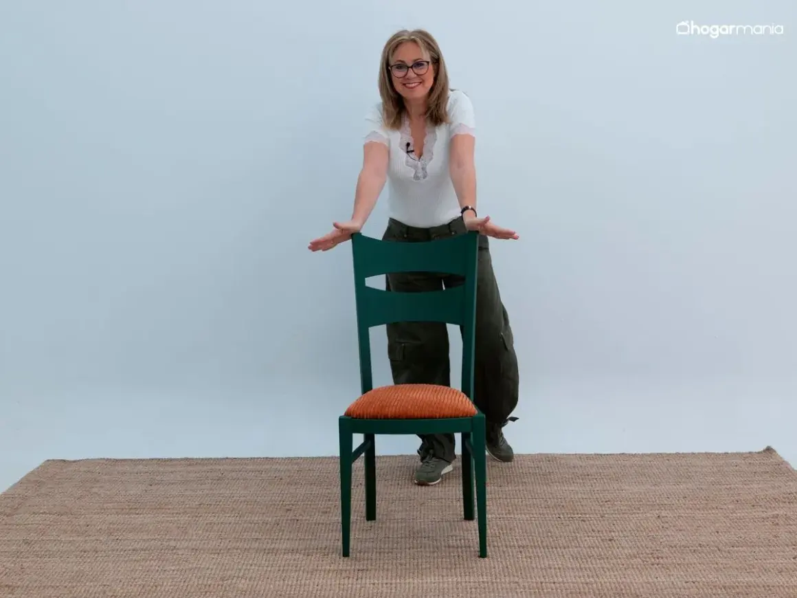 Mujer sonriente muestra cómo forrar sillas con estilo, usando una silla verde con cojín naranja.