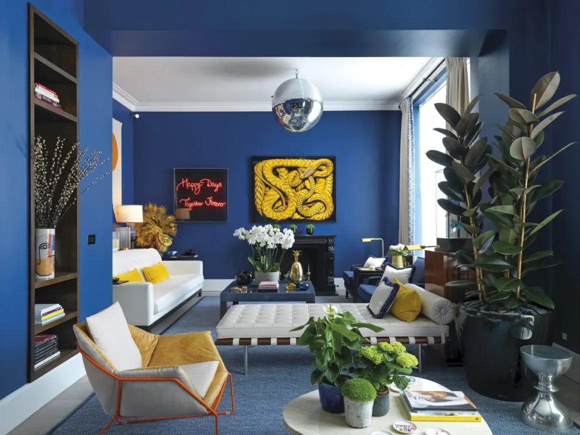 El azul vibrante de las paredes crea un telón de fondo audaz. El amarillo mostaza y el blanco puro son colores que combinan con el azul, aportando calidez y luminosidad a este salón moderno.