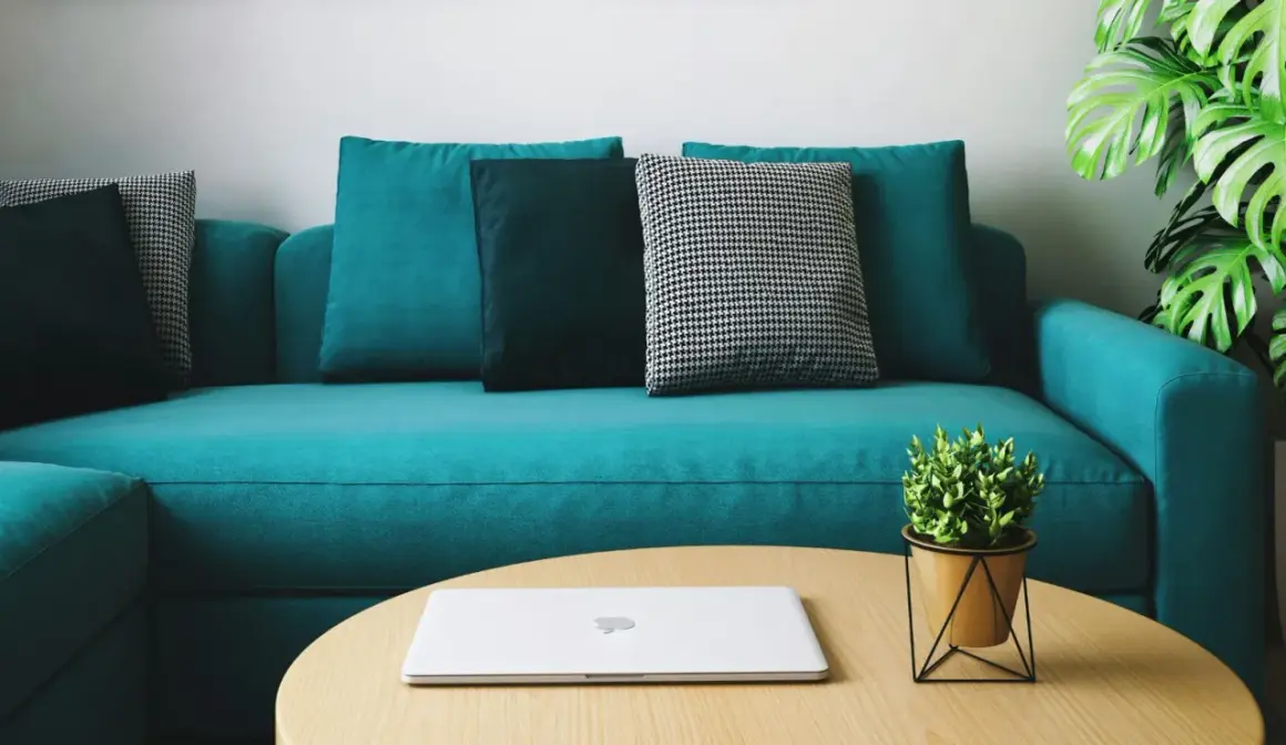 Un sofá moderno color turquesa, con cojines en tonos oscuros y un patrón de pata de gallo. Un portátil y una planta decoran la mesa de centro. ¡Perfecto para teñir el sofá de un nuevo color!