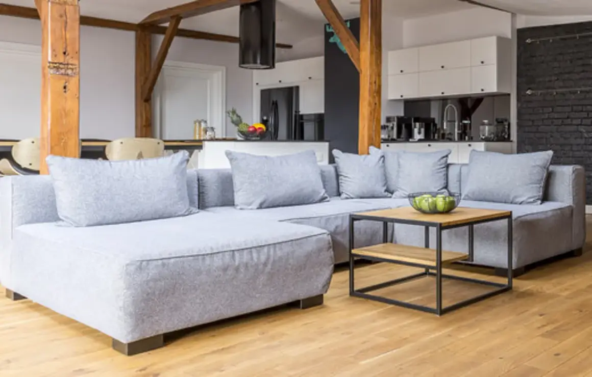 Sofá gris moderno con cojines, mesa de centro de madera y metal. Ideas para como hacer fundas de sofas faciles.