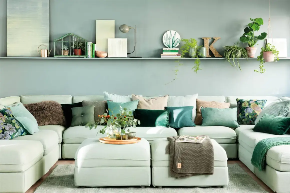 Sofá modular con cojines en tonos verdes y marrones, creando una paleta de colores que combinan con turquesa. Plantas y objetos decorativos en una estantería superior.