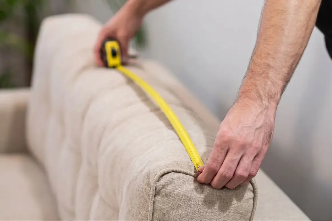 Persona mide un sofá con cinta métrica para saber como medir sofá para fundas.