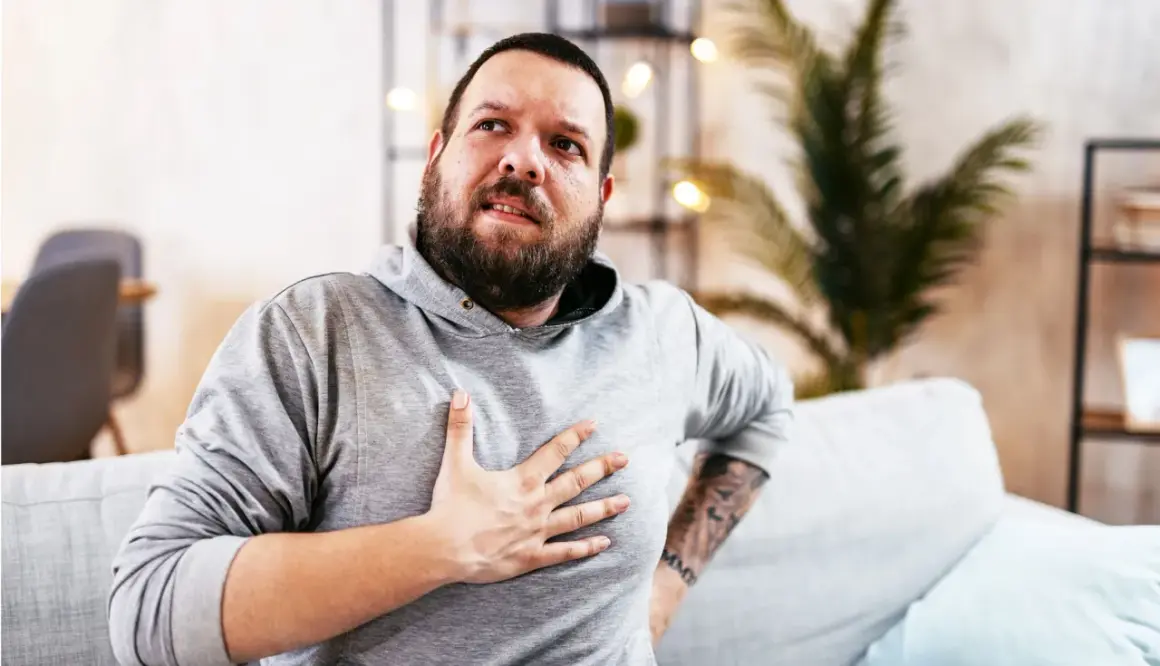 Hombre con barba, con la mano en el pecho, con expresión de dolor. Estaba durmiendo y de repente me desperté sin poder respirar.