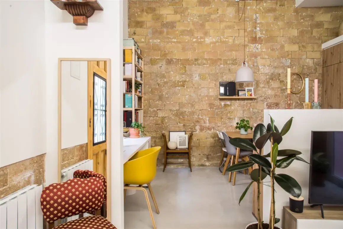 Acogedor loft de 40 metros cuadrados con pared de ladrillo visto, comedor, zona de trabajo y plantas.