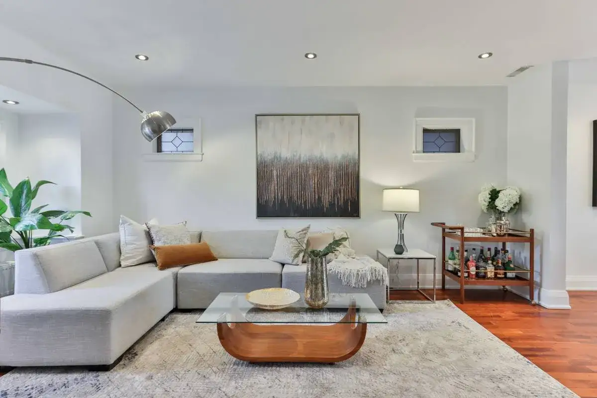 Elegante sal&oacute;n con sof&aacute; modular gris y beige, mesa de centro de cristal y madera, y un carrito de bar.