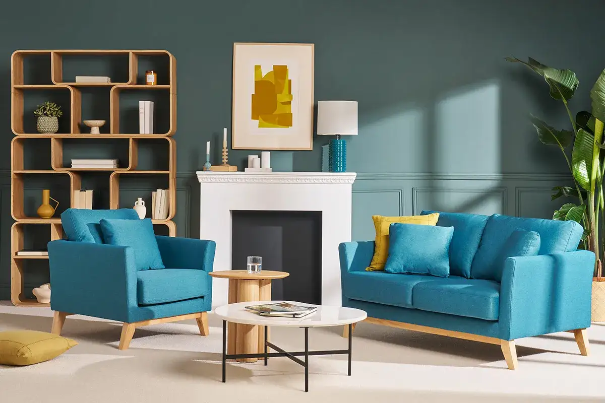 Sof&aacute; y sill&oacute;n en azul petr&oacute;leo, combinaci&oacute;n perfecta con estanter&iacute;a de madera y detalles amarillos.