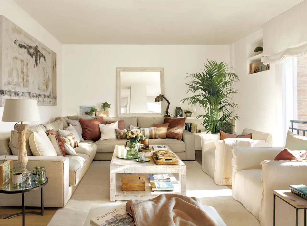 Sof&aacute; esquinero beige con cojines coloridos, mesa de centro de madera, plantas y cuadro abstracto. Ideas de que poner al lado del sofa para un sal&oacute;n acogedor.