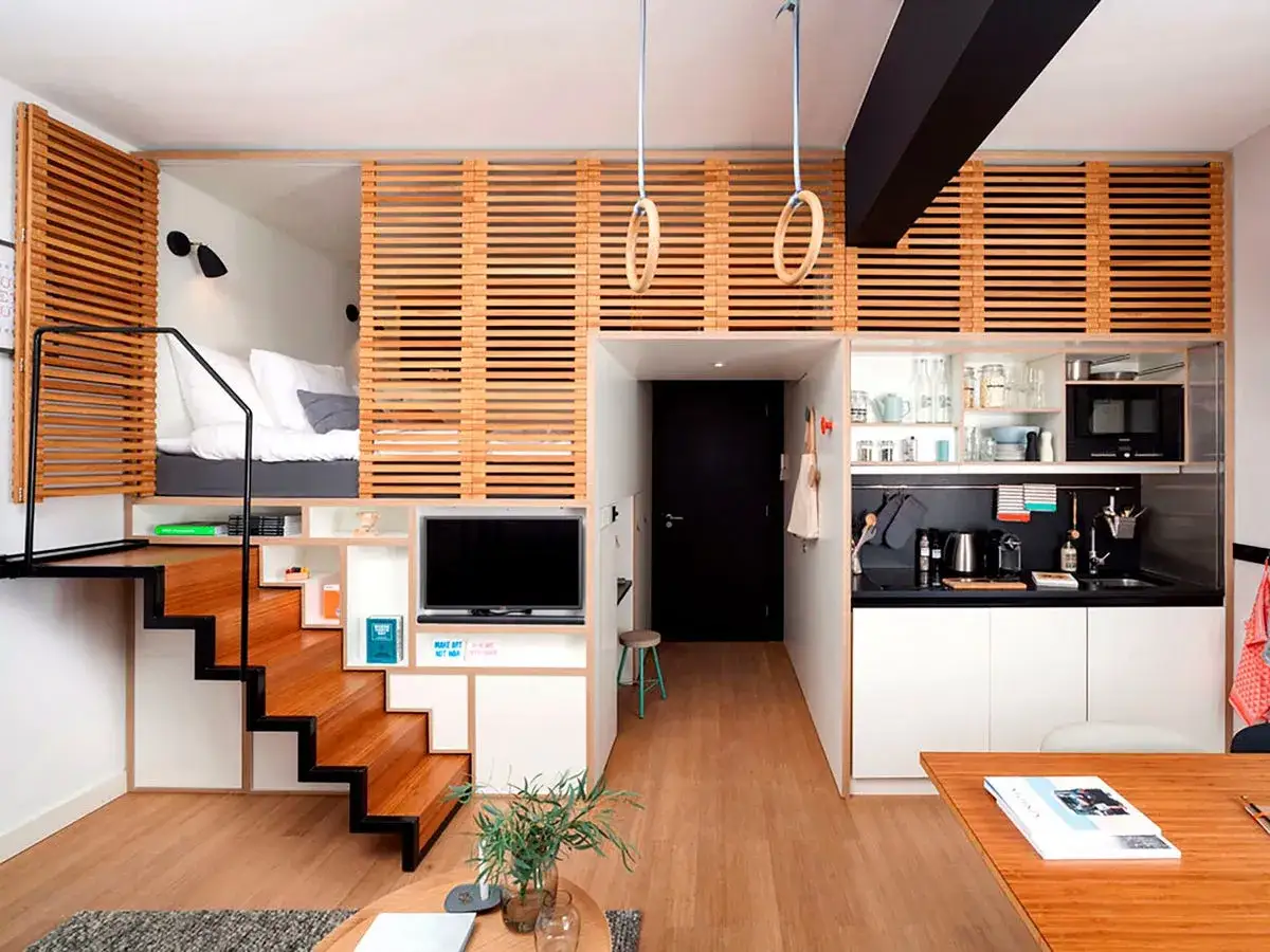 Acogedor loft de 40 metros cuadrados con cama elevada, escaleras de madera, cocina compacta y zona de estar.