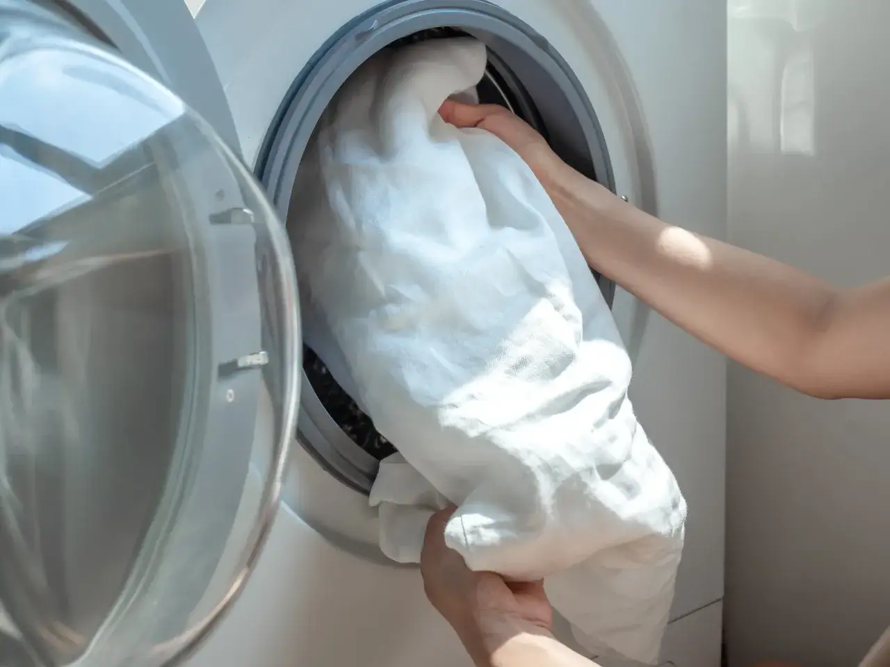 Manos colocando ropa blanca en la lavadora.