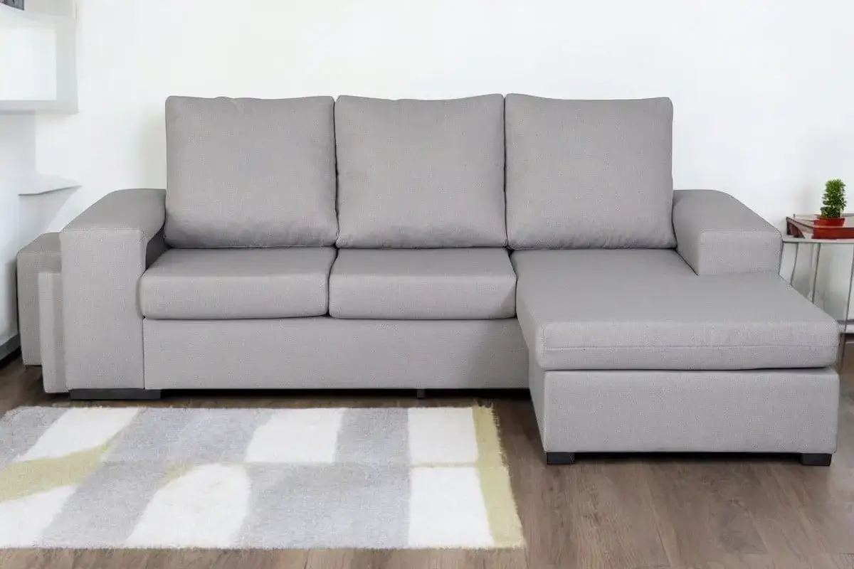 Sofá modular gris con chaise longue a la derecha, ideal para relajarse.