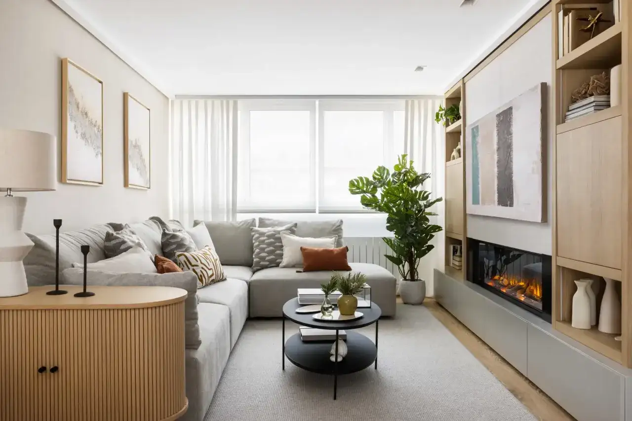 Un sal&oacute;n moderno con un sof&aacute; esquinero gris y un sof&aacute; individual, ideal para saber como colocar dos sofas en un salon peque&ntilde;o. Chimenea y estanter&iacute;as de madera.