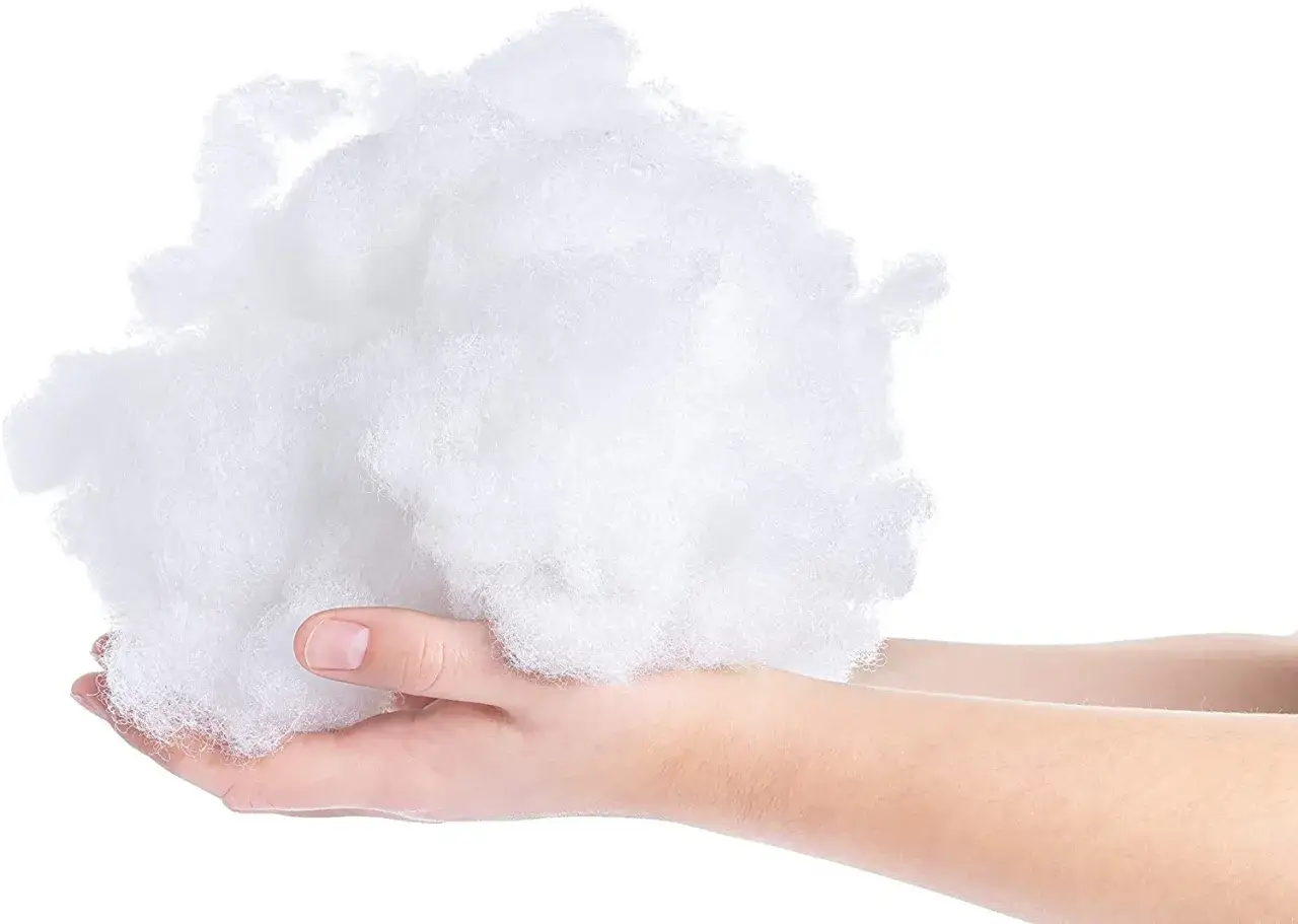 Mano sostiene una nube de fibra hueca siliconada, material esponjoso y blanco, ideal para relleno.