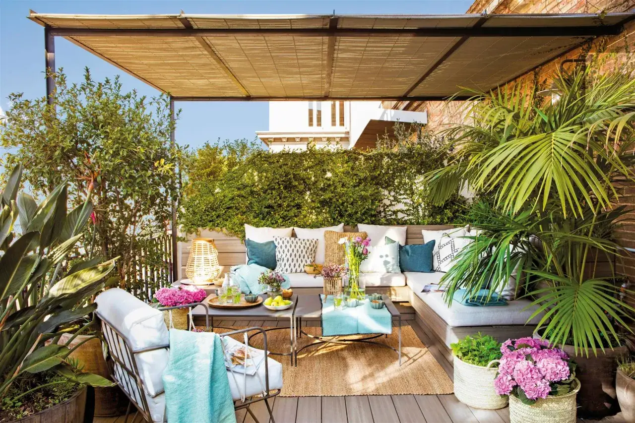 Sofá de terraza con cojines y plantas, creando un espacio acogedor. Ideas para separar terrazas con vegetación y mobiliario.