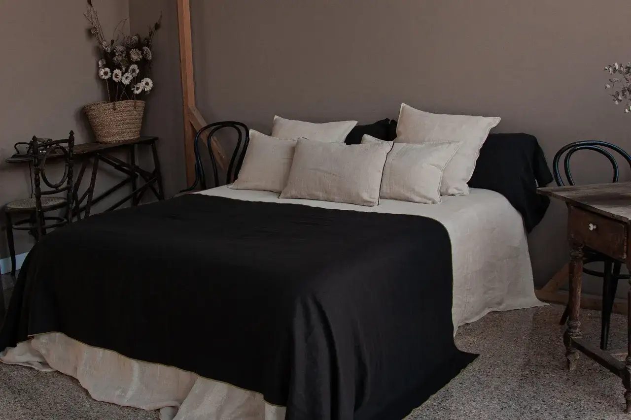 Cama con ropa de cama de lino y lino lavado en tonos neutros. La diferencia entre lino y lino lavado se aprecia en la textura suave y arrugada del segundo.