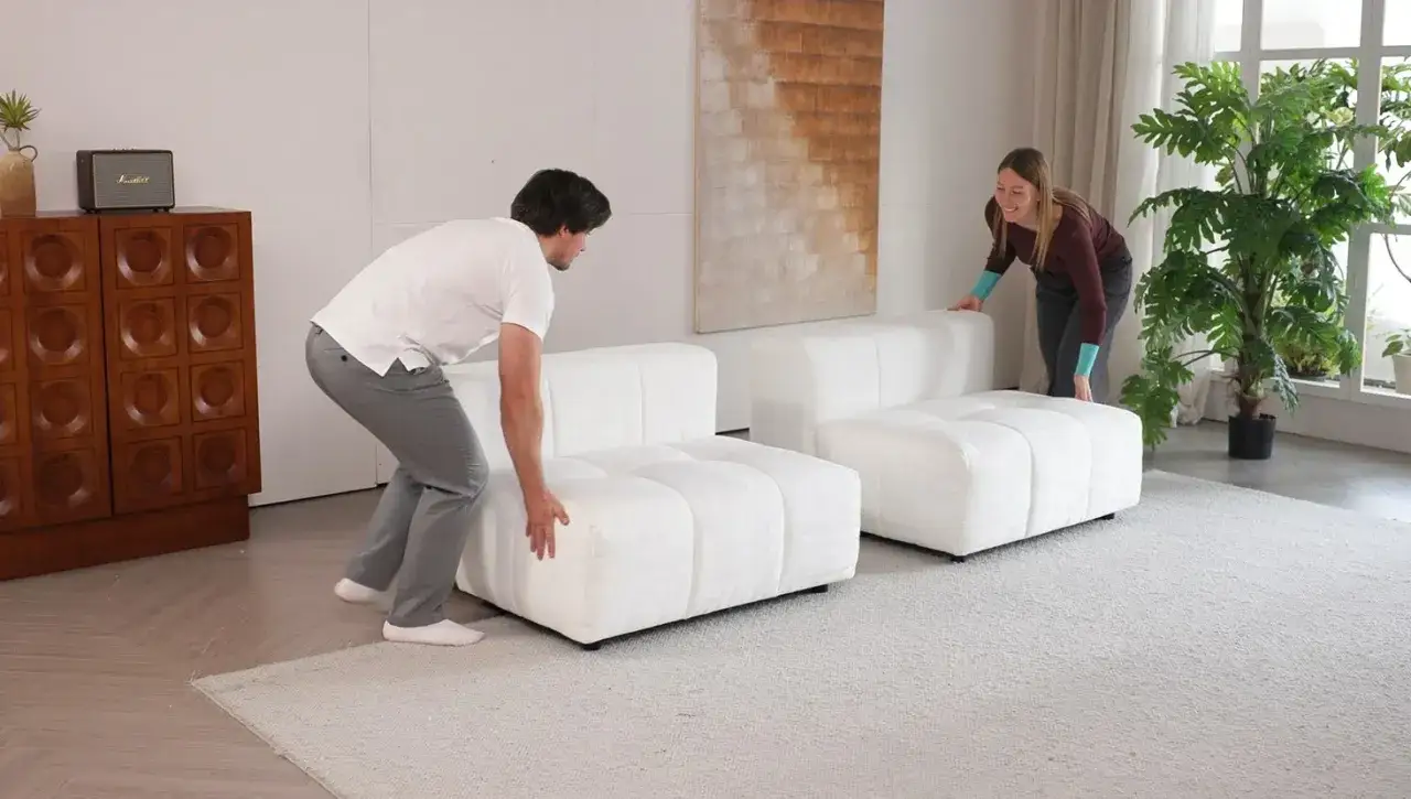 Pareja moviendo m&oacute;dulos de sof&aacute; blanco para desmontar chaise longue.