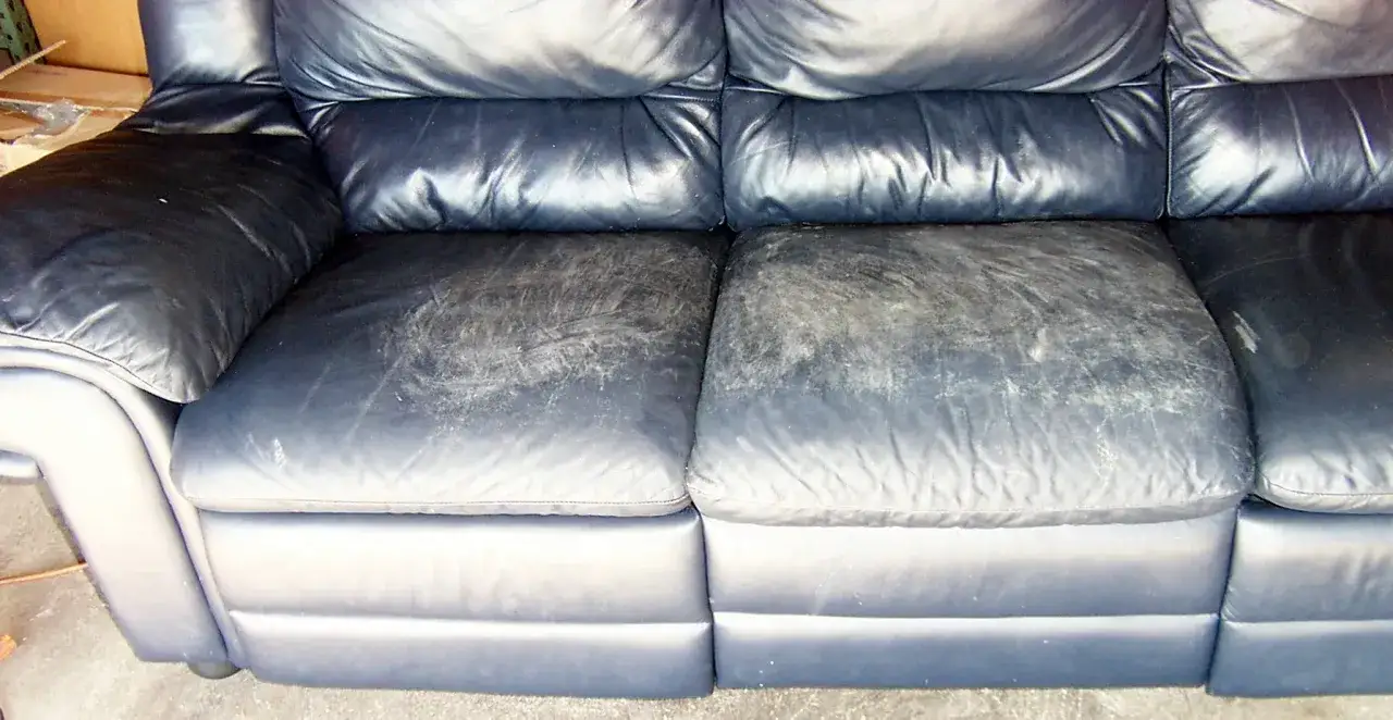 Sofá de cuero azul con asientos desgastados y agrietados, listos para reparar cuero agrietado y devolverles la vida.