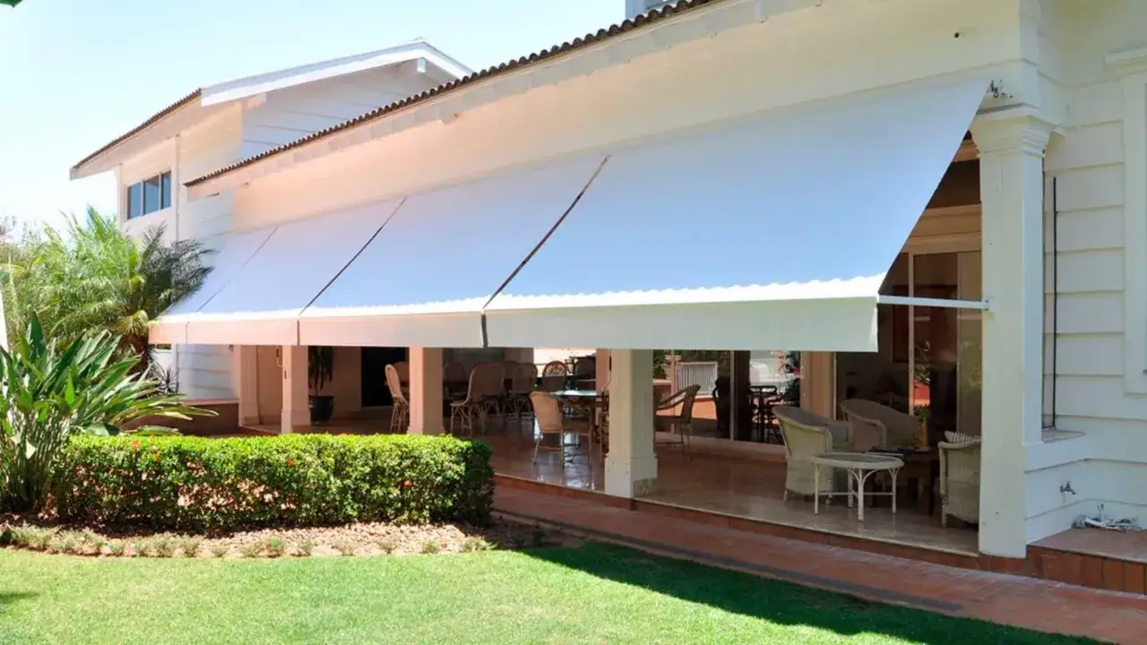 Amplia lona blanca cubre el porche de una casa, creando un espacio sombreado con muebles de exterior.