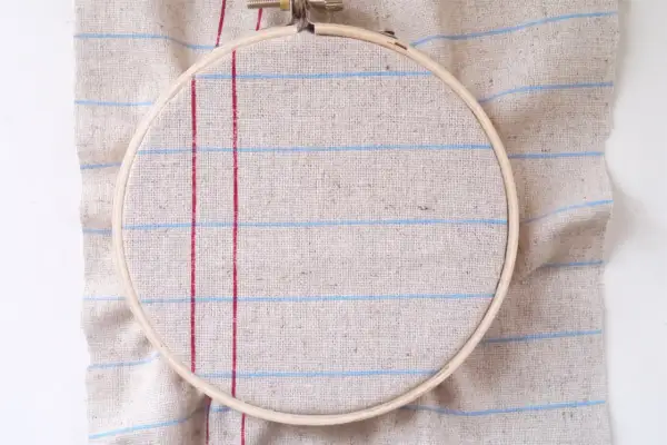 Bastidor de bordar sobre tela de lino con líneas rojas y azules, ideal para tus proyectos de hogar manualidades para casa.