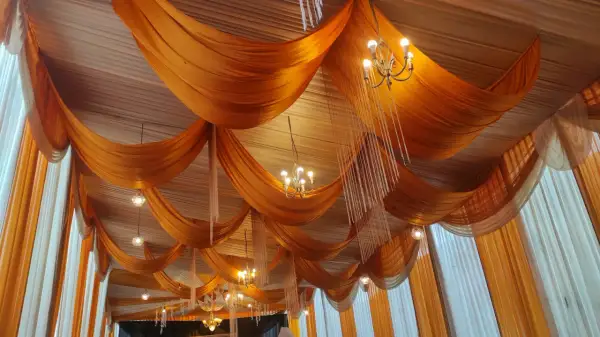 Techo con telas naranjas y blancas, adornado con candelabros y colgantes de cristal.