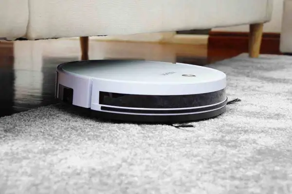 Robot aspirador blanco y negro limpiando alfombra gris, ideal para saber como eliminar los acaros del hogar.