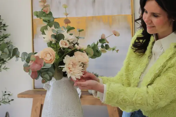 Mujer sonriente arregla un ramo de flores de tela, mostrando cómo limpiar flores de tela para mantener su belleza.