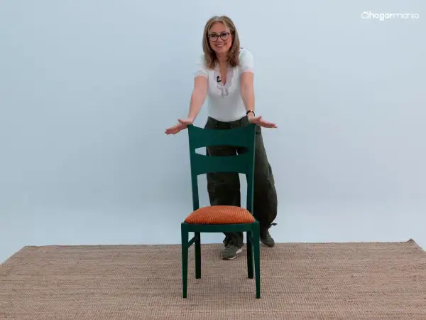 Mujer sonriente muestra cómo forrar sillas con estilo, usando una silla verde con cojín naranja.