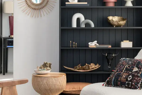 Estantería oscura con objetos decorativos en tonos tierra y dorados, mezclando muebles de distintos colores y texturas para un estilo ecléctico.