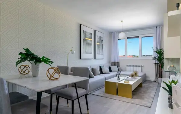 Salón rectangular dos ambientes con mesa de mármol, sofá modular gris y mesas doradas.