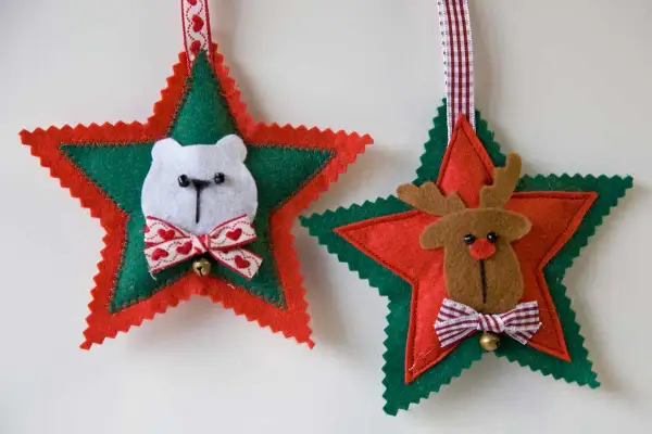 Adornos navideños de fieltro: un oso polar y un reno adornan estrellas rojas y verdes, listos para colgar.
