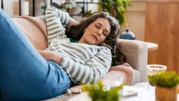 Mujer descansando en el sofá, con los ojos cerrados, lista para dormir antes de comer.