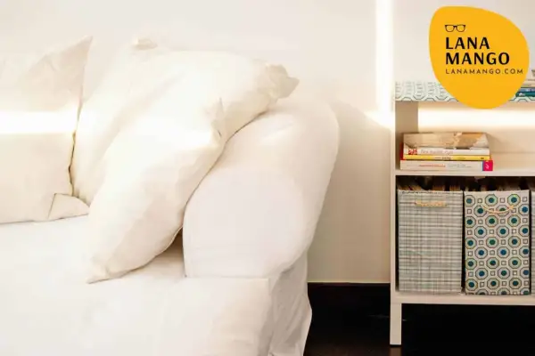 Sofá blanco con cojines y estantería con libros y cestas. Ideas para como hacer funda sofa.