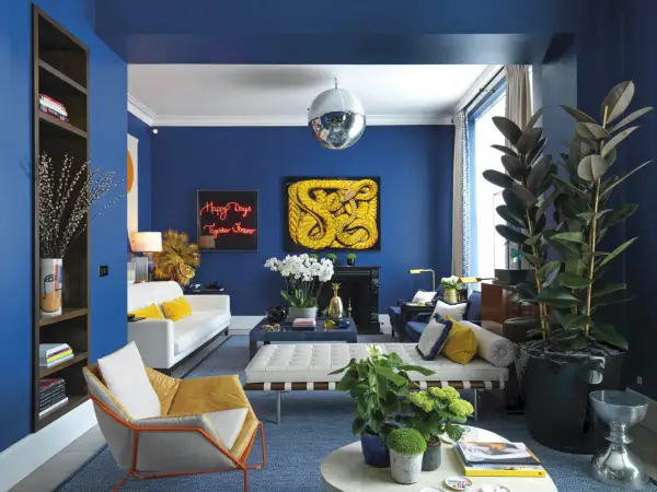 El azul vibrante de las paredes crea un telón de fondo audaz. El amarillo mostaza y el blanco puro son colores que combinan con el azul, aportando calidez y luminosidad a este salón moderno.