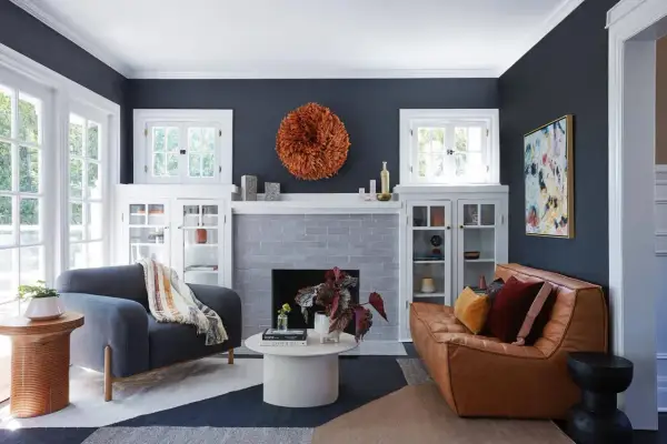 Ideas para decorar rincones pequeños: un sofá de cuero, sillón gris, chimenea y arte abstracto en un salón moderno.