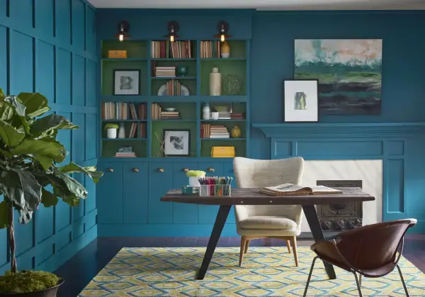 Estudio con paredes y estanterías en azul petróleo, combinación perfecta con detalles verdes. Alfombra geométrica y mobiliario moderno.