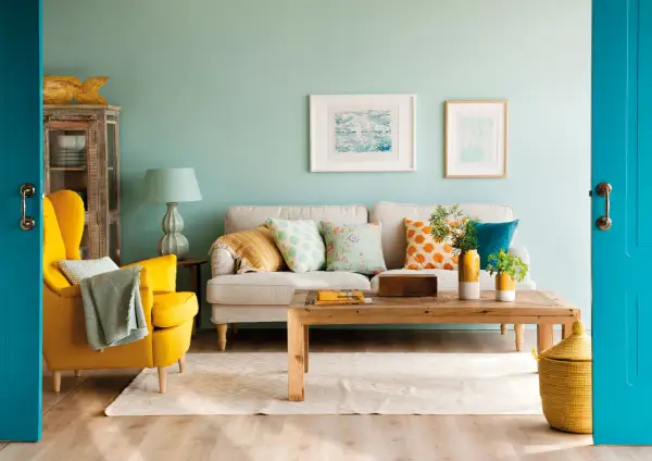 Un salón moderno donde se combinan mostaza y azul en cojines, sillón y puerta.