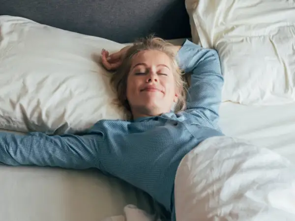 Mujer rubia sonríe plácidamente en su cama, disfrutando de un sueño reparador bajo la suave roba de llit.