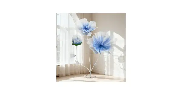 Tres flores de tela grandes, azules y blancas, con tallos blancos, junto a una ventana con cortinas.