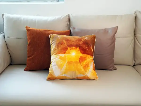 Tres cojines sobre un sofá de cuero: uno naranja texturizado, uno con un diseño de cristal amarillo brillante y otro marrón. El cojín central, con su estampado de velour que es, irradia calidez.