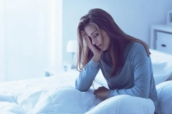 Mujer en la cama, con la mano en la frente, parece que me duermo y me despierto a cada rato.