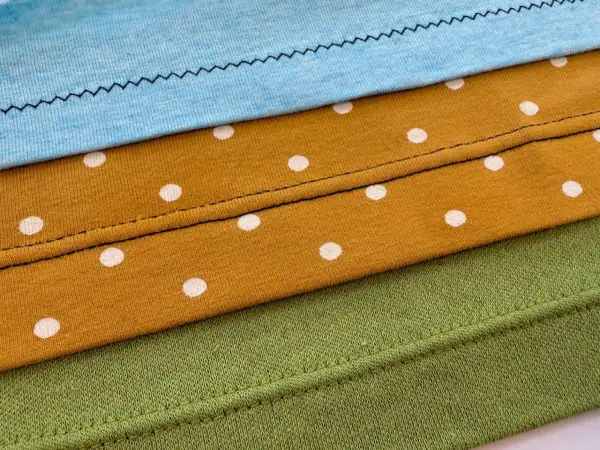 Demostración de como hacer un dobladillo en tela de punto con diferentes puntadas y telas: azul, mostaza con lunares blancos y verde.