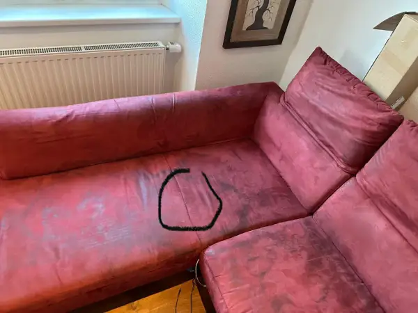 Un sofá de tela rojo con una mancha negra en forma de círculo. ¿Cómo reparar un sofá de tela roto?