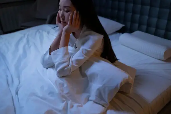 Me despierto de madrugada y no puedo volver a dormir. Una mujer sentada en la cama, con las manos en la cara, mirando al vacío.
