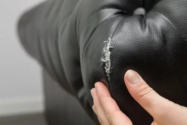 Mano examinando un desgarro en cuero negro, mostrando la necesidad de reparar cuero agrietado.