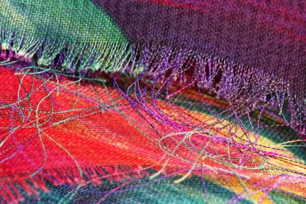 Detalle de tela con hilos sueltos de colores vibrantes. Se aprecia el tejido y cómo se puede coser a mano para que no se deshilache.