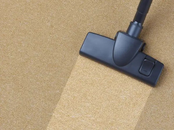 Cabezal de aspiradora limpiando una alfombra beige. Aprende como limpiar la alfombra en casa para un hogar impecable.