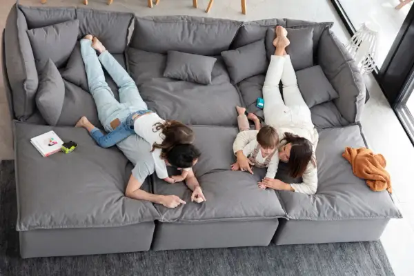 Familia jugando en un cómodo sofá gris. Los niños se divierten sobre sus padres mientras descansan en este amplio sofá.
