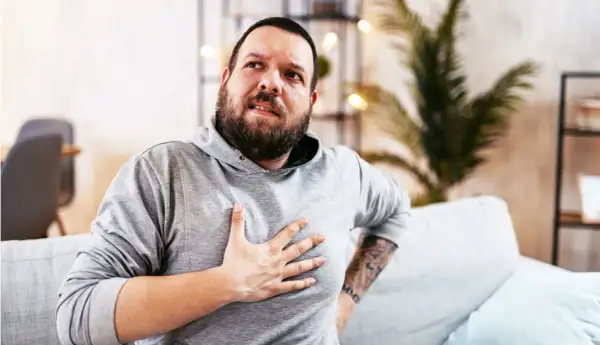 Hombre con barba, con la mano en el pecho, con expresión de dolor. Estaba durmiendo y de repente me desperté sin poder respirar.